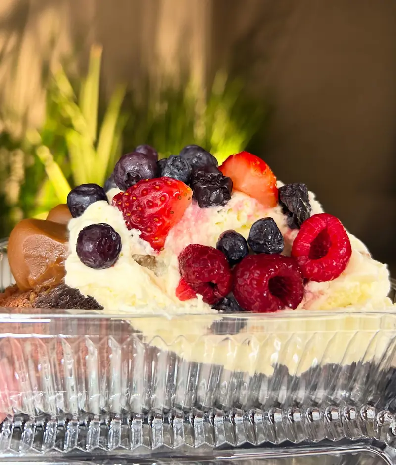 Brownie con crema, dulce de leche, frutillas, frambuesas y arándanos, en bandeja de vidrio