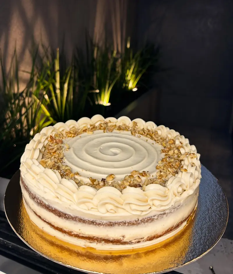 Carrot cake entera con frosting blanco y nueces, sobre base dorada