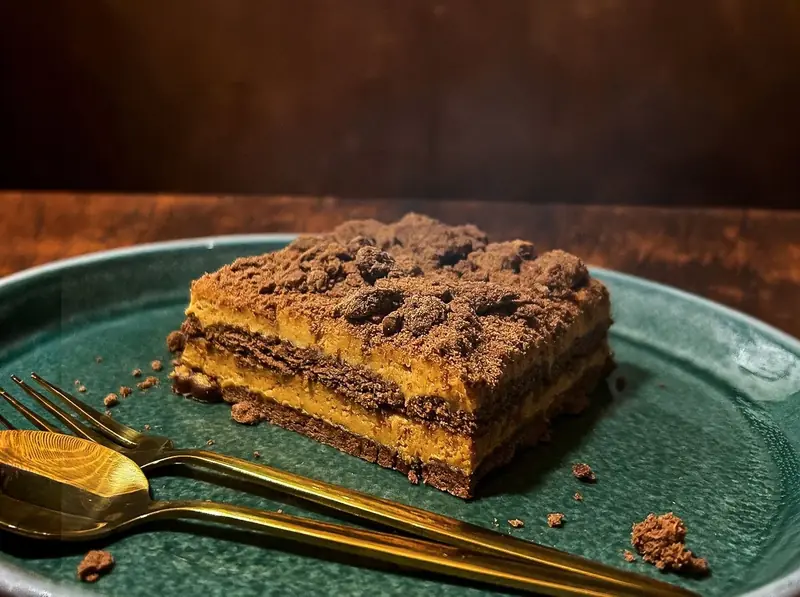 Porción de chocotorta con crumble de galletitas y cubiertos dorados